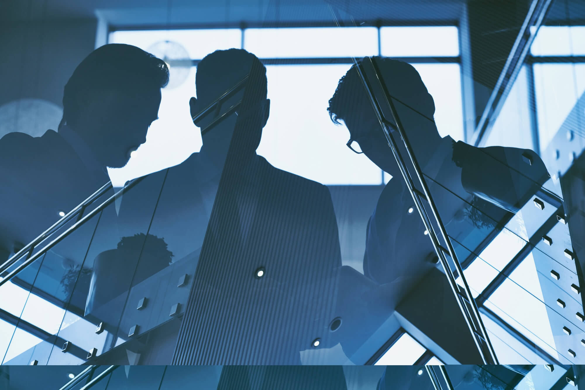 Silhouettes of three businesspeople having a discussion in a modern glass office.